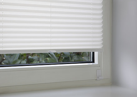 White pleated blind fixed with an angle bracket into the window frame, close-up of the lower mount.
