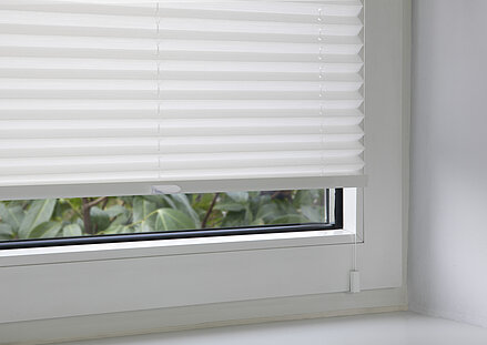 White pleated blind attached with a window clip at the lower part of the window frame.