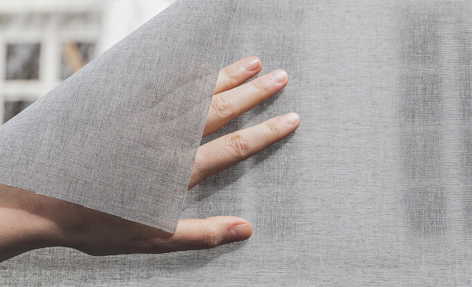 Hand slightly peels back textured SQUID® adhesive textile from the glass.