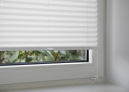 White pleated blind mounted using a clamp bracket on the window sash, showing the lower fixing.