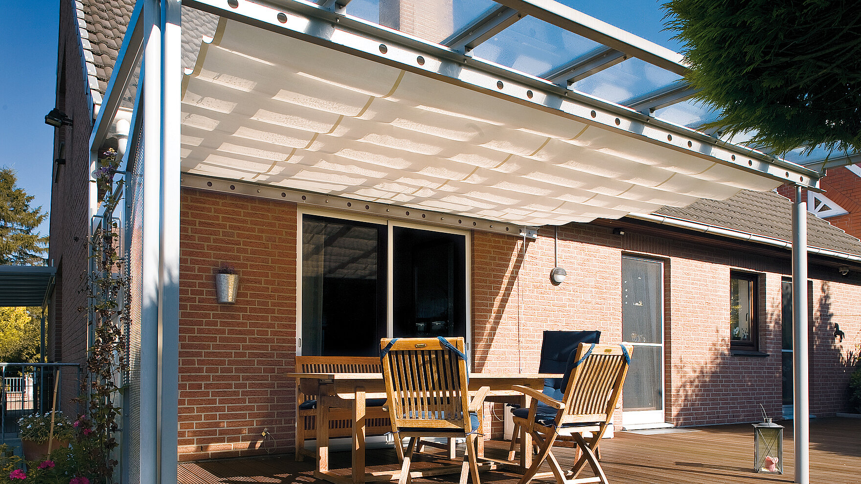 Interior pleated awning beneath glass roof provides shade over furnished wooden patio.
