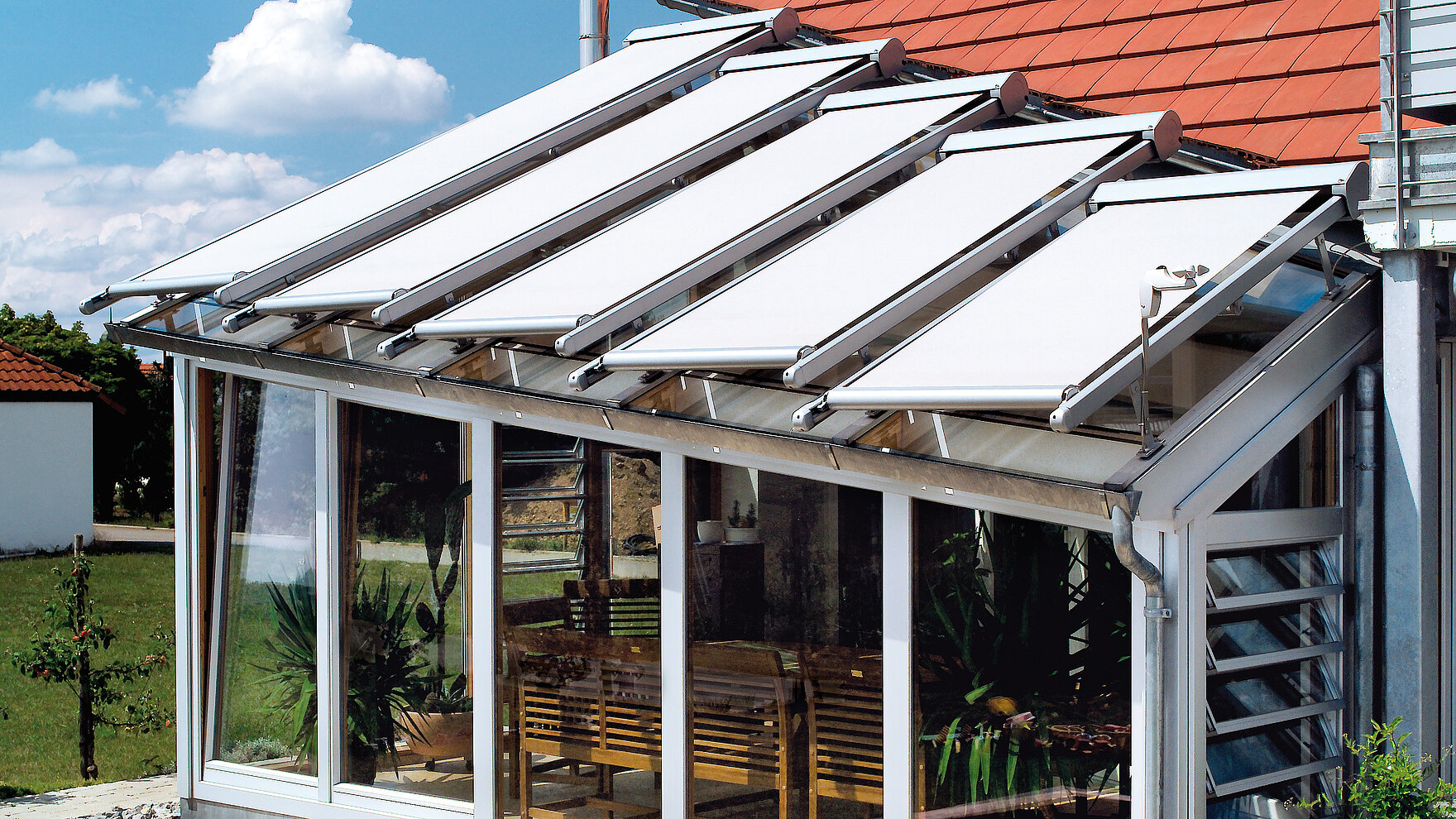 Conservatory with exterior roof shading using separately guided white awning fabrics.