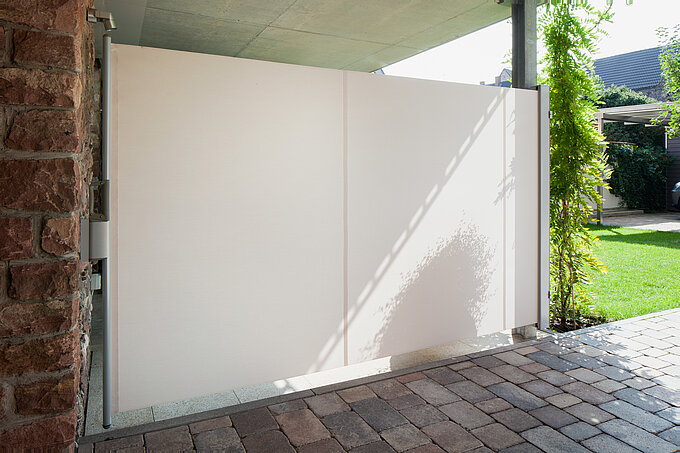Fully extended side awning used as a privacy screen on a patio with garden view.