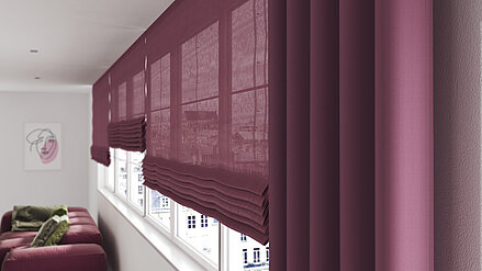 Elegante halbtransparente Raffrollos und ein passender Vorhang in dunklem Beeren-Ton, harmonisch kombiniert in einem stilvollen Wohnraum.