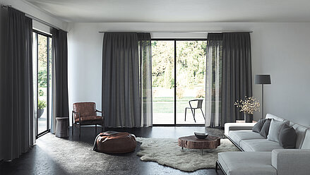Wohnzimmer mit bodentiefen Fenstern und dunklen MHZ Vorhängen in Anthrazit als Sicht- und Sonnenschutz.