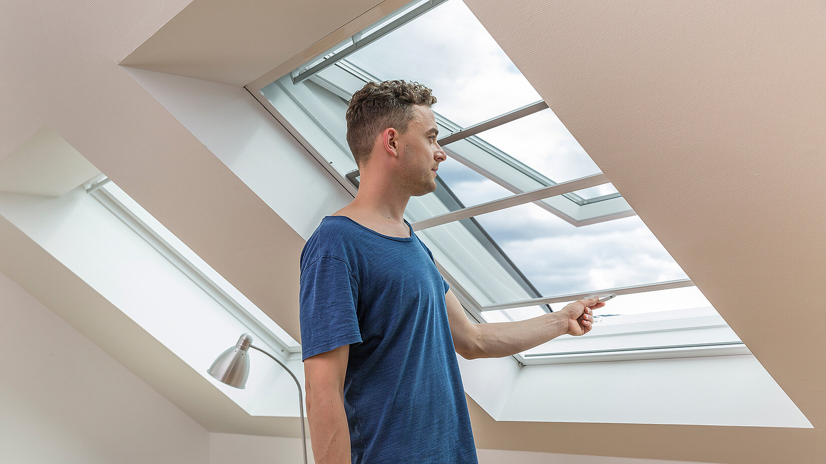 Man slides insect screen frame across open roof window.