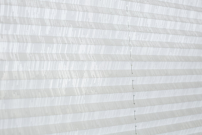 Detailaufnahme eines weißen Plisseestoffs mit feinem Streifenmuster und sichtbarer Schnurführung.