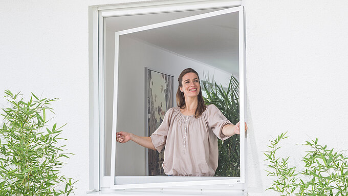 Woman installs insect screen tension frame from inside into an open window.