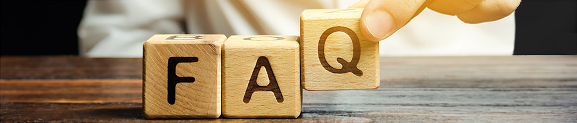 Drei Holzwürfel mit den Buchstaben F, A und Q, eine Hand stellt den Q-Würfel auf