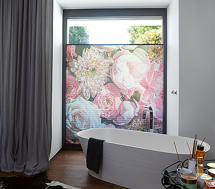 Plissee mit großem Blumenmotiv im Badezimmer als halbtransparenter Sichtschutz vor bodentiefem Fenster