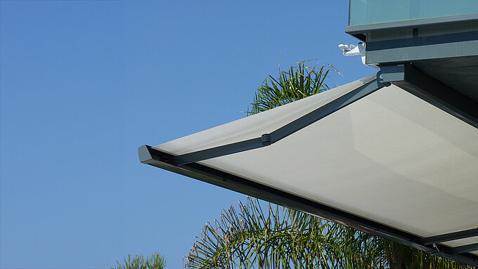 Seitlicher Blick auf ausgefahrene Gelenkarmmarkise mit klar sichtbarer Mechanik vor blauem Himmel.