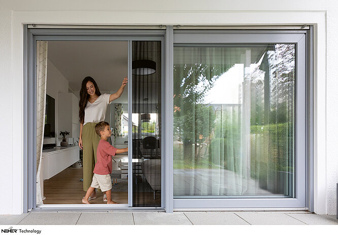 Woman and child open pleated insect screen on large patio sliding door.