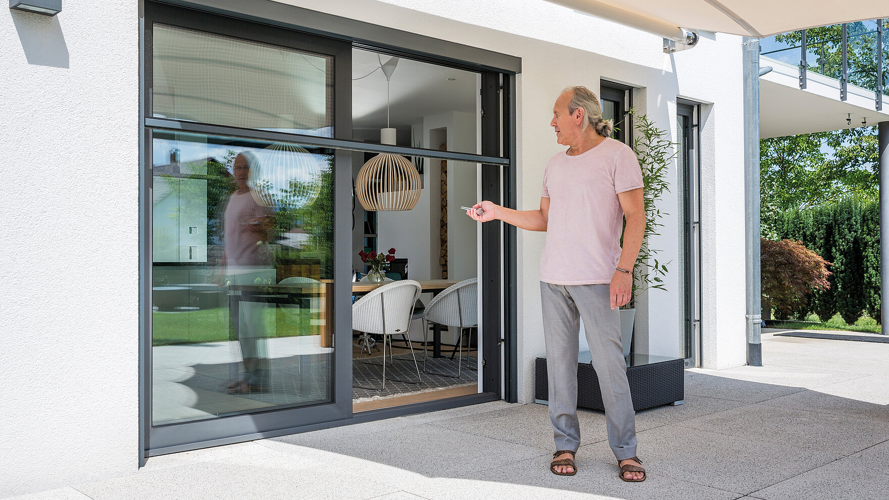 Mann steuert per Fernbedienung ein elektrisches Insektenschutzrollo an einer Terrassentür.