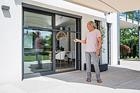 Mann steuert per Fernbedienung ein elektrisches Insektenschutzrollo an einer Terrassentür.