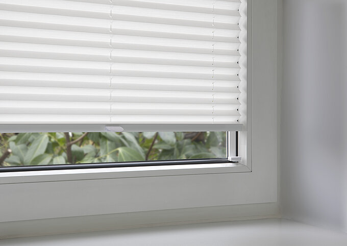 Weißes Plissee mit Klebeset in der Glasleiste eines Fensters montiert, Detailaufnahme.