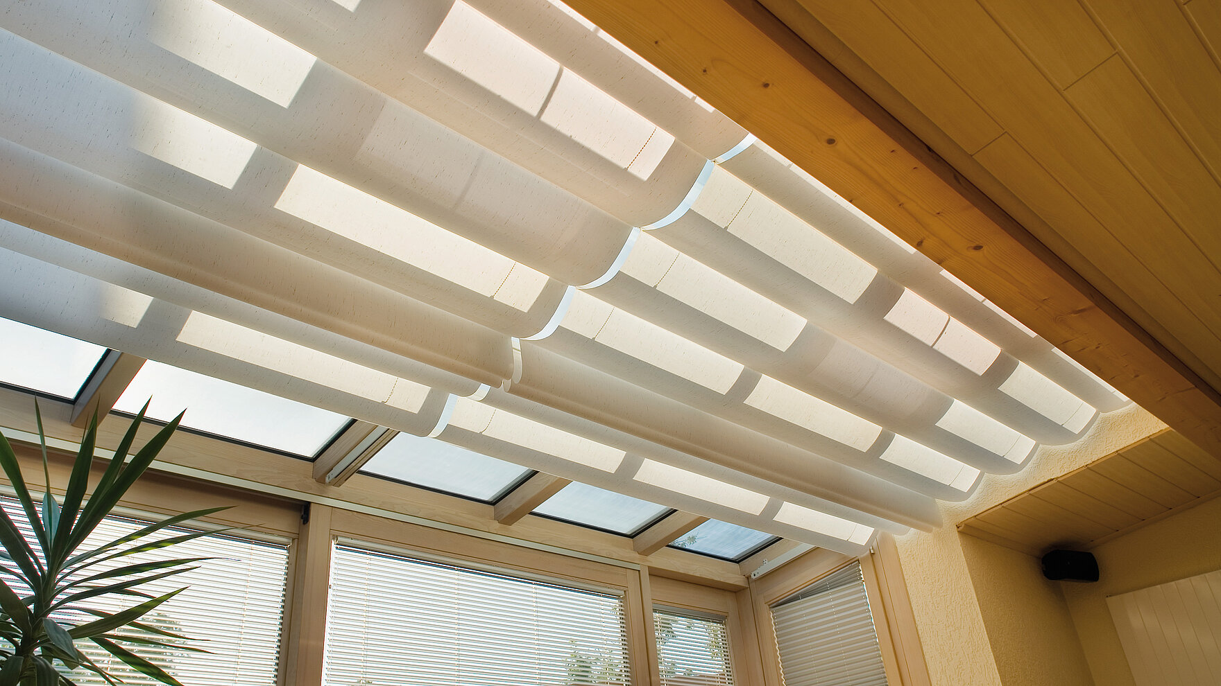 Interior conservatory shading with white pleated fabric mounted beneath glass roof.