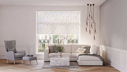 Wohnzimmer mit floral gemustertem, halbtransparentem Rollo vor französischen Fenstern. Helles Sofa, grauer Ohrensessel und moderne Hängelampe runden das Design ab.