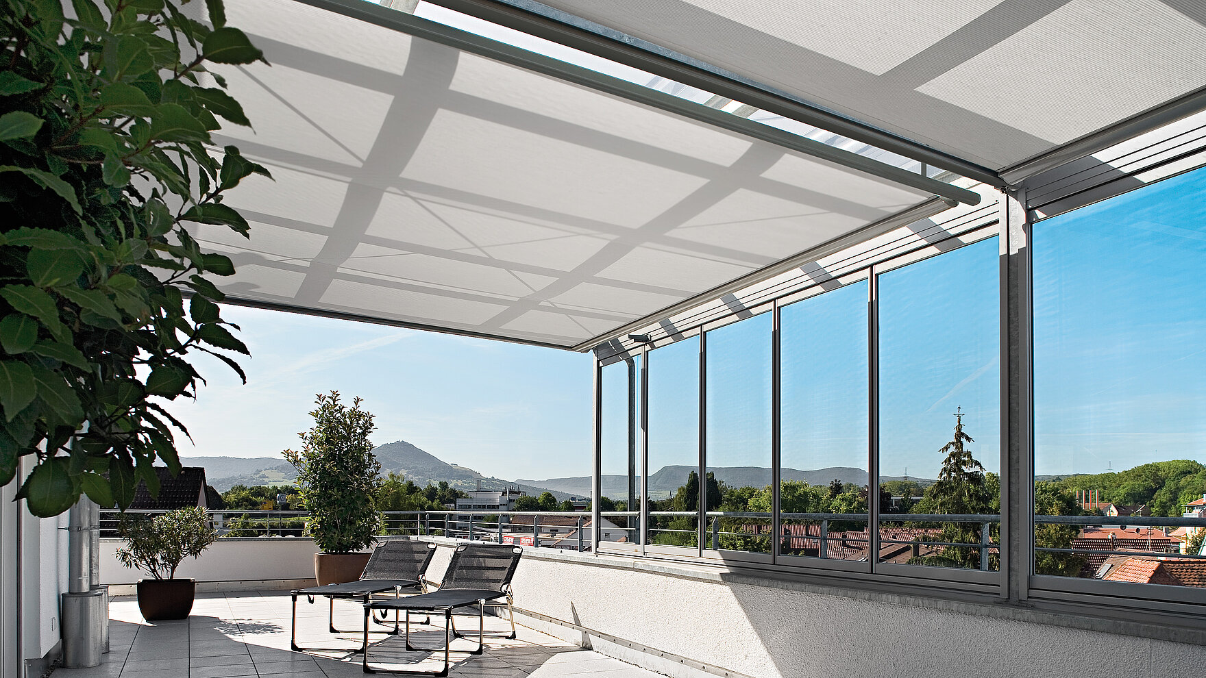 Interior awning system beneath a glass roof on a rooftop terrace with scenic view.