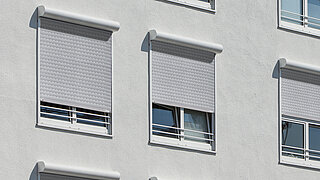 Mehrere geschlossene MHZ Rollläden an der Fassade eines modernen Wohnhauses.