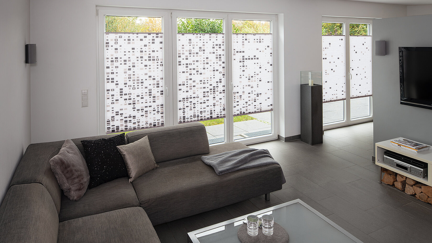 Living room with MHZ Code honeycomb blinds featuring a geometric square pattern in black, grey, and white.