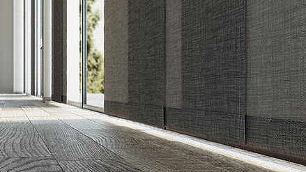 Dunkle textile Flächenvorhänge vor großen Fenstern in einem modernen Innenraum mit Holzoptik-Boden.