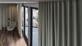 Detailansicht eines strukturierten, grauen MHZ-Vorhangs vor raumhohem Fenster in einem modernen Schlafzimmer.