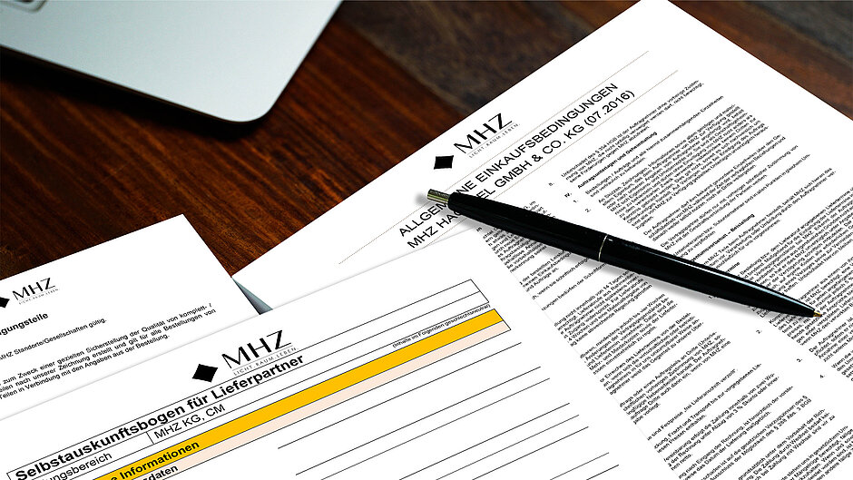 Printed MHZ supplier documents: self-assessment and purchasing terms on a desk.