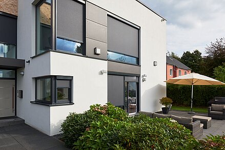 Modernes Wohnhaus mit geschlossenen Senkrechtmarkisen an großen Fenstern und Terrasse mit Sonnenschirm.