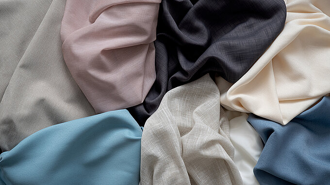 Hochwertige Stoffe in verschiedenen Farben, darunter Beige, Rosa, Schwarz, Creme, Blau und Grau, kunstvoll drapiert.