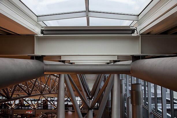 MHZ-Beschattungssystem auf Stahlträgern unter dem Glasdach des Flughafens Hamburg mit Blick auf die Halle darunter.